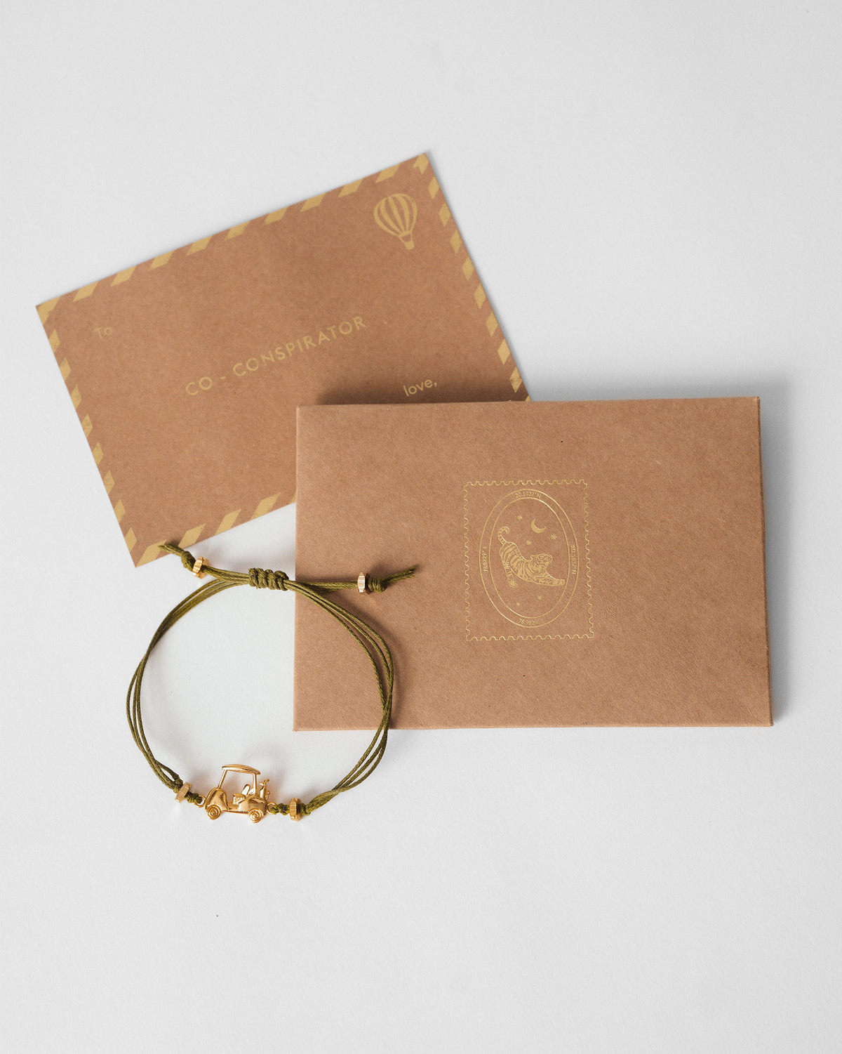 Golf Cart Rakhi in olive green cord beside brown kraft envelopes.