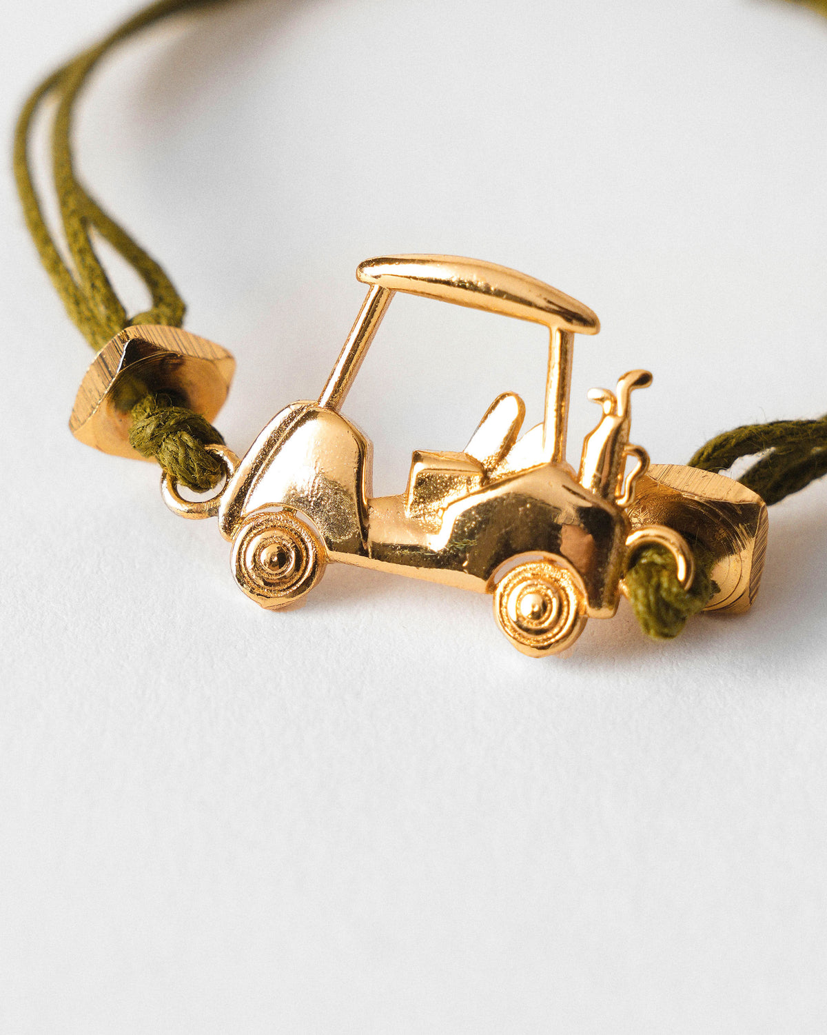 Close-up of a Golf Cart Rakhi with a gold golf cart charm on olive green cord.