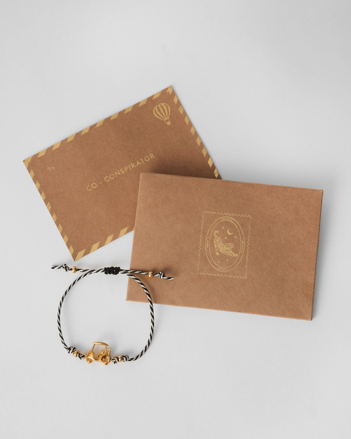 Golf Cart Rakhi in black and white thread beside brown kraft envelopes.