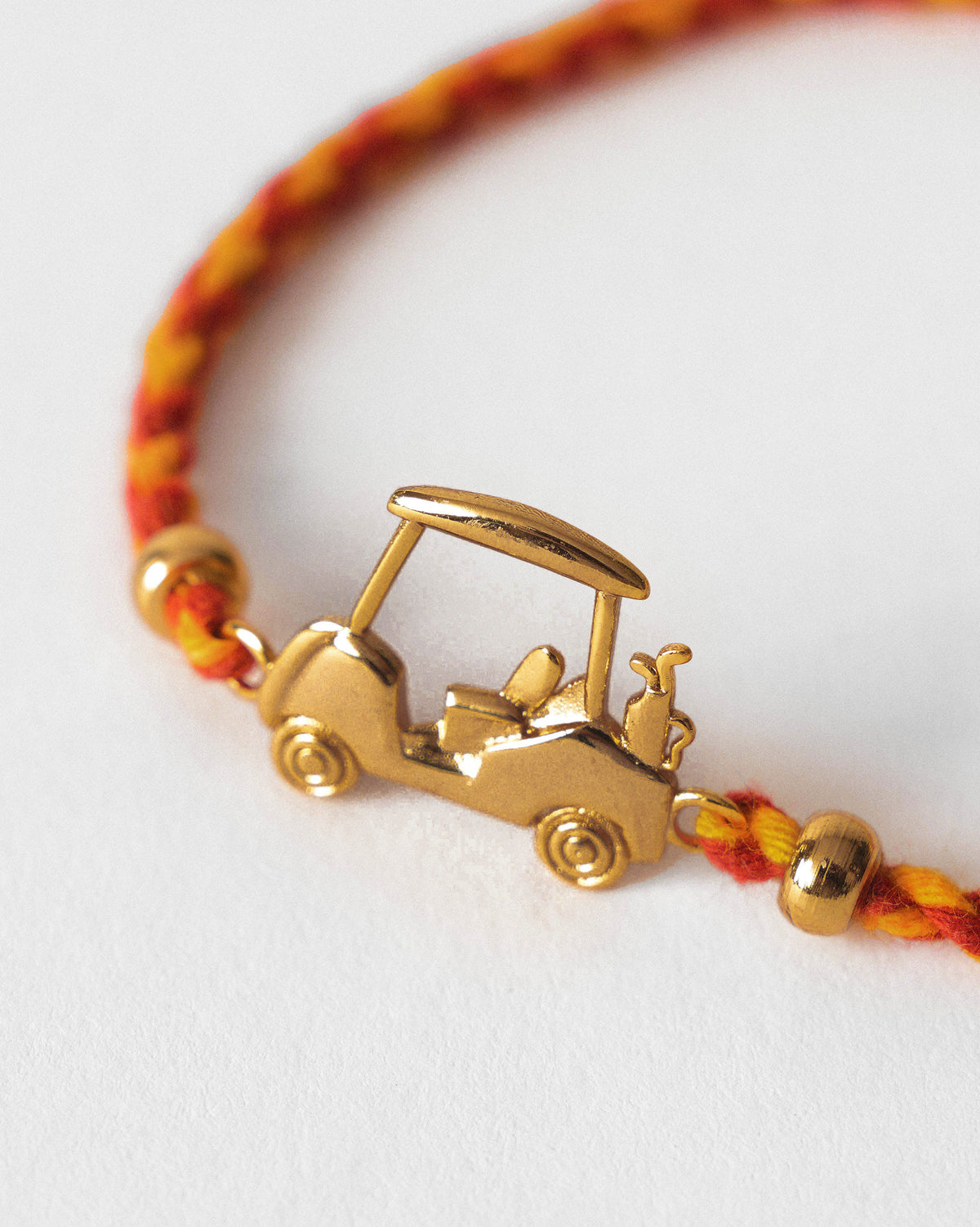 Close-up of a Golf Cart Rakhi with a gold golf cart charm on red and orange braid.