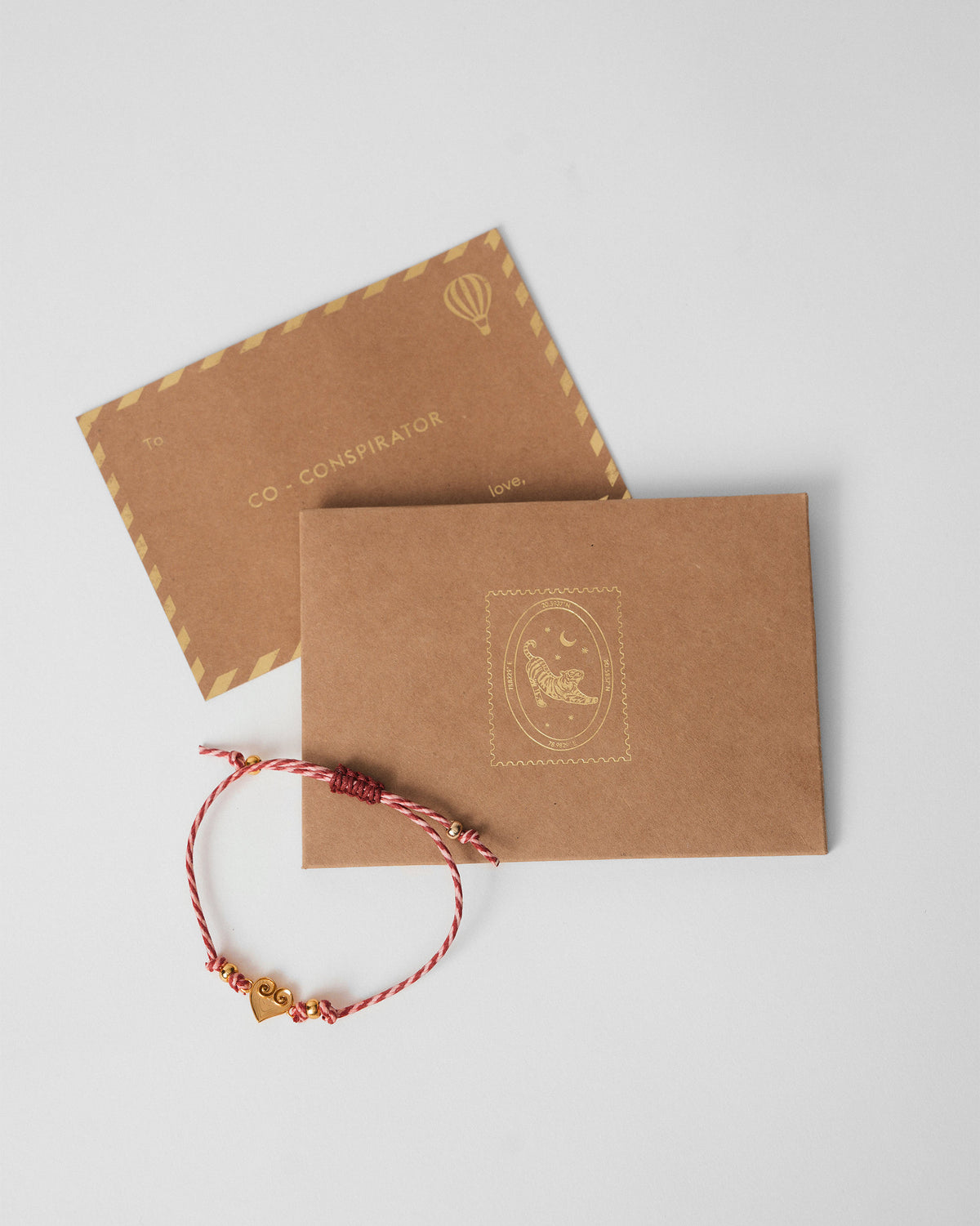 Dil Rakhi in red and white stripes beside brown kraft envelopes.