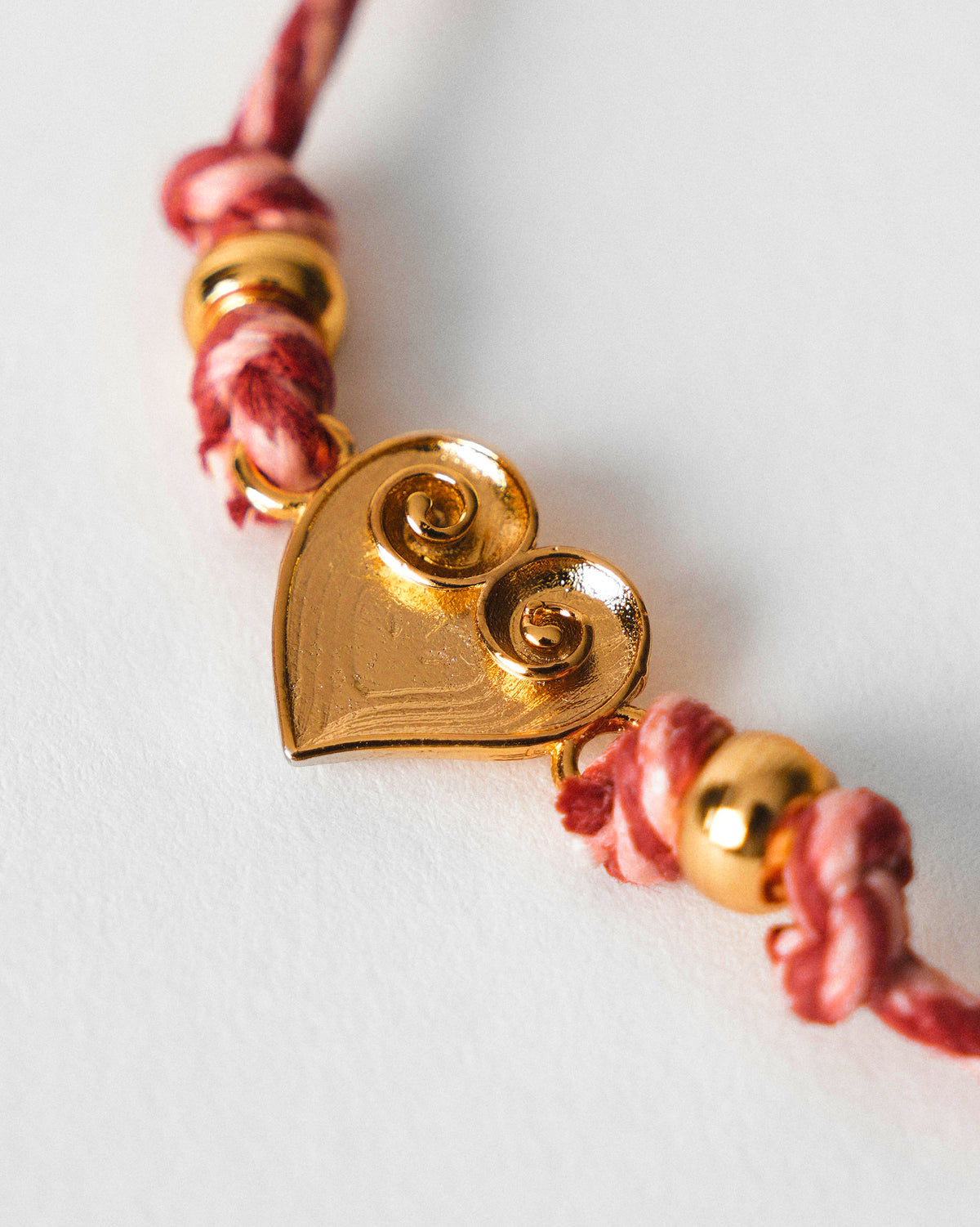 Close-up of a gold heart charm on pink and red braided thread.