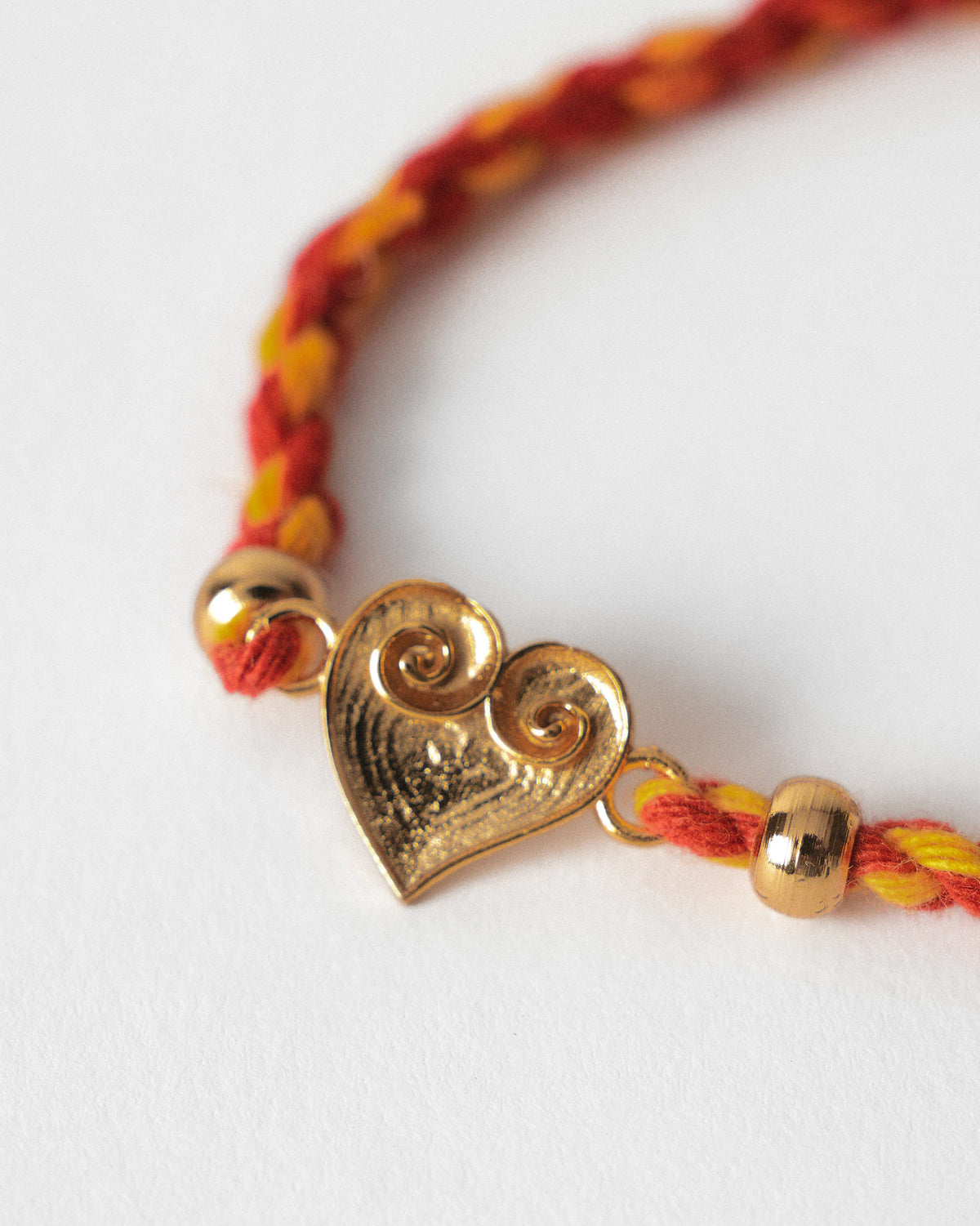 Close-up of a Dil Rakhi heart charm on red and orange braided thread.