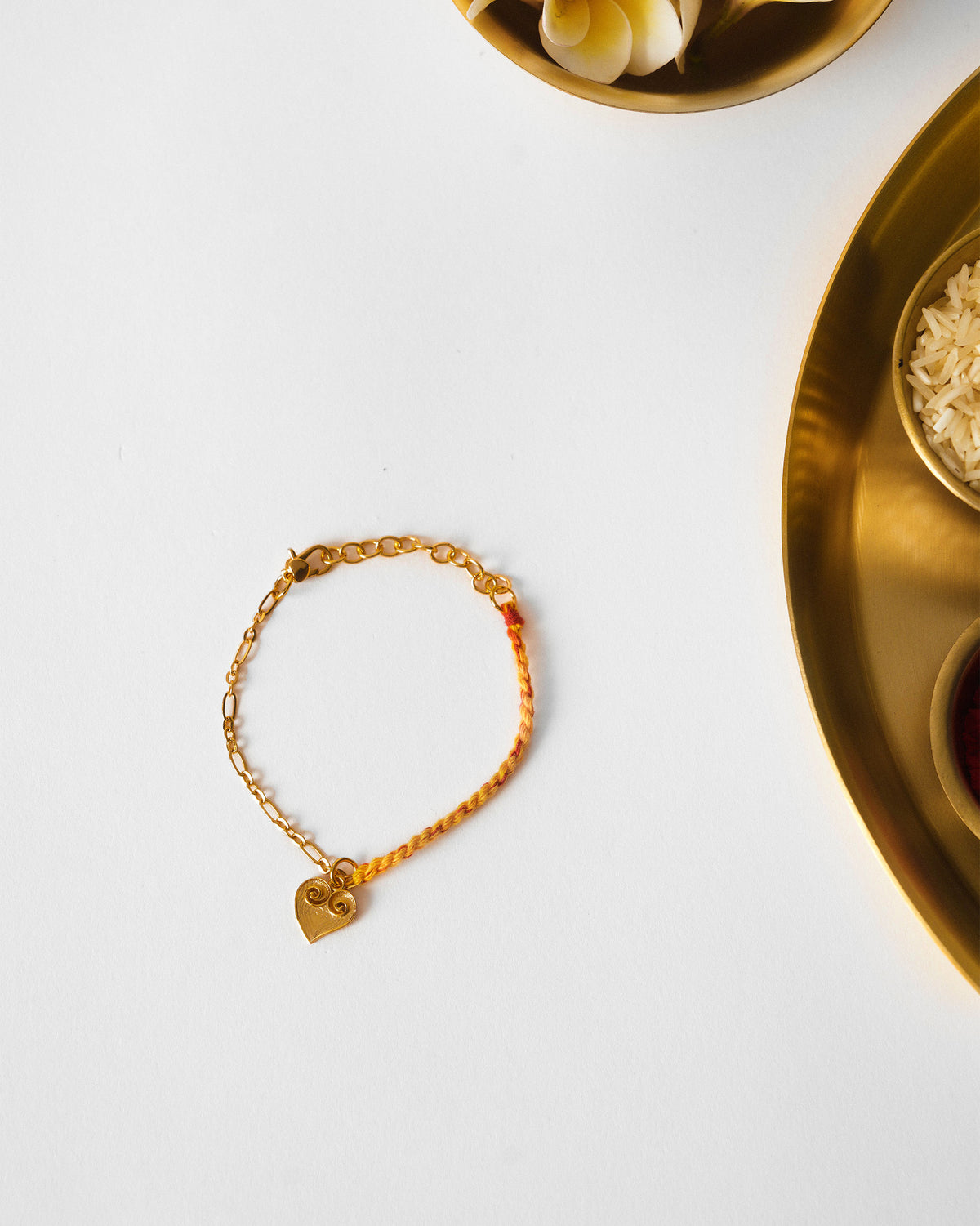 Dil Charmlet in gold and red with a heart charm laid flat.