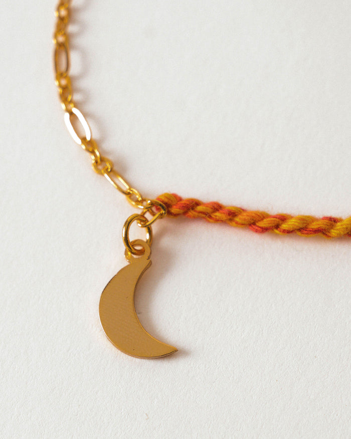 Close-up of Crescent Charmlet showing a gold crescent charm on a red and orange cord.