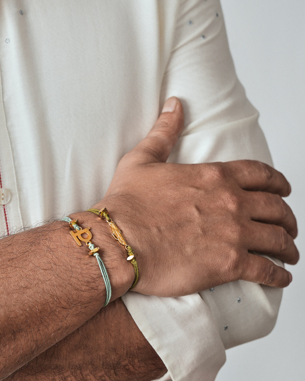 Person wearing an Alphabet V Rakhi in pale green cord with a gold charm on the wrist.