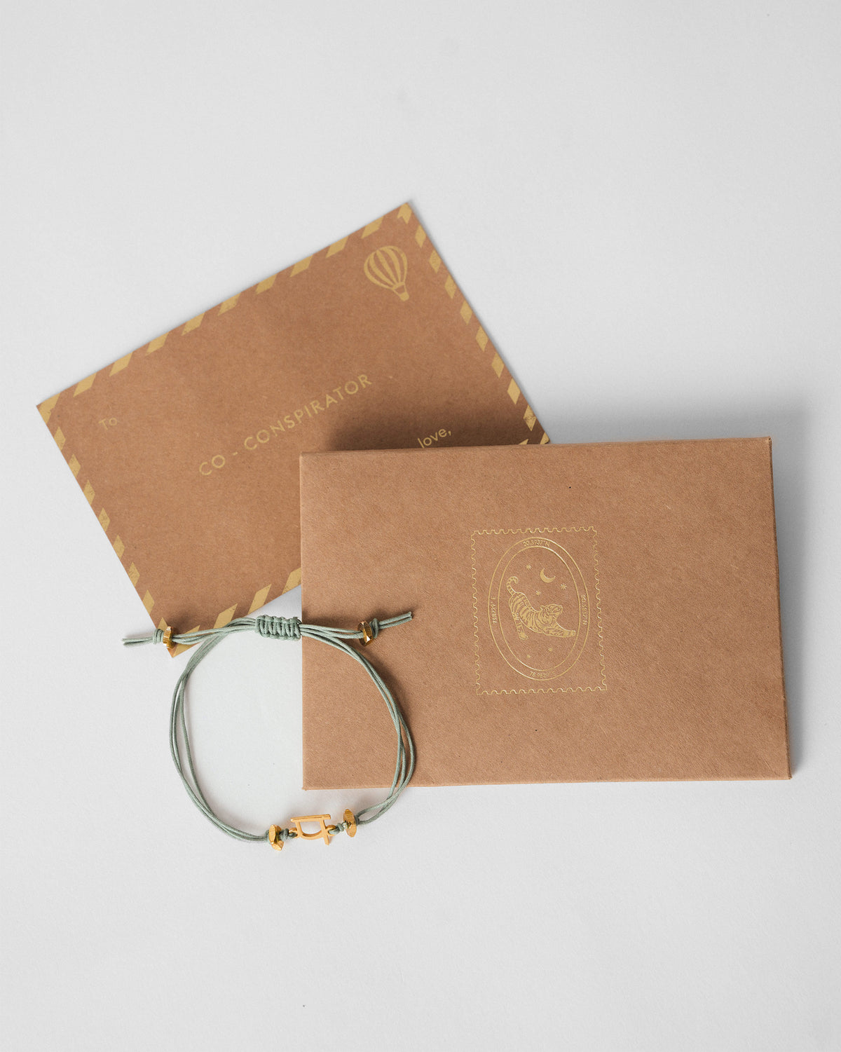 Alphabet P Rakhi with a gold charm, shown beside its kraft card envelope.