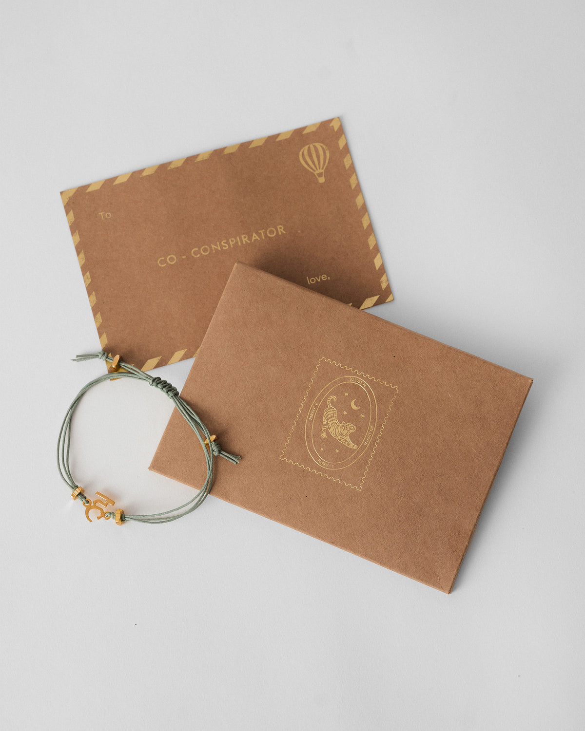 Alphabet H Rakhi beside a kraft envelope and card.