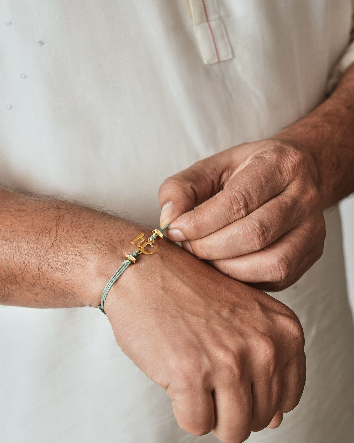 Person wearing Alphabet H Rakhi with a gold charm on the wrist.