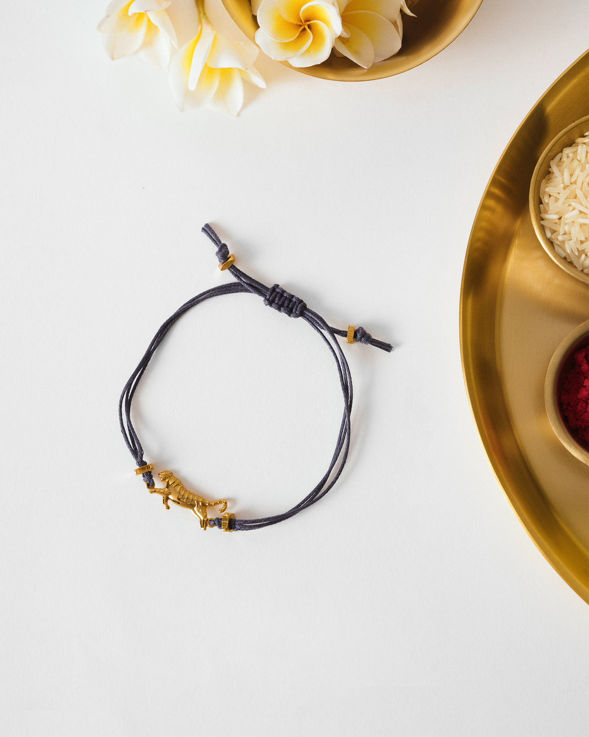 Blue tiger rakhi with a gold tiger charm laid flat beside a thali.