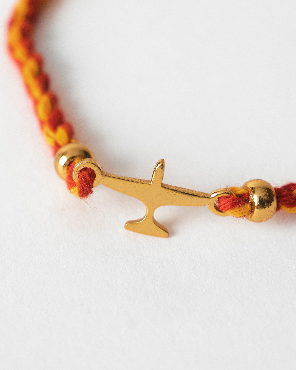 Close-up of Airplane Rakhi showing a gold airplane charm on red and gold braided cord.