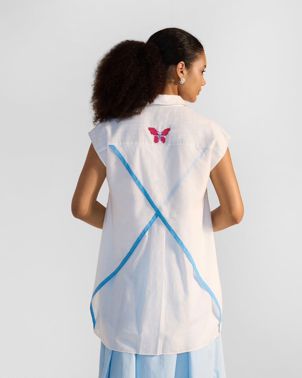 Back of a white Eira top with a butterfly and crossing blue tapes.
