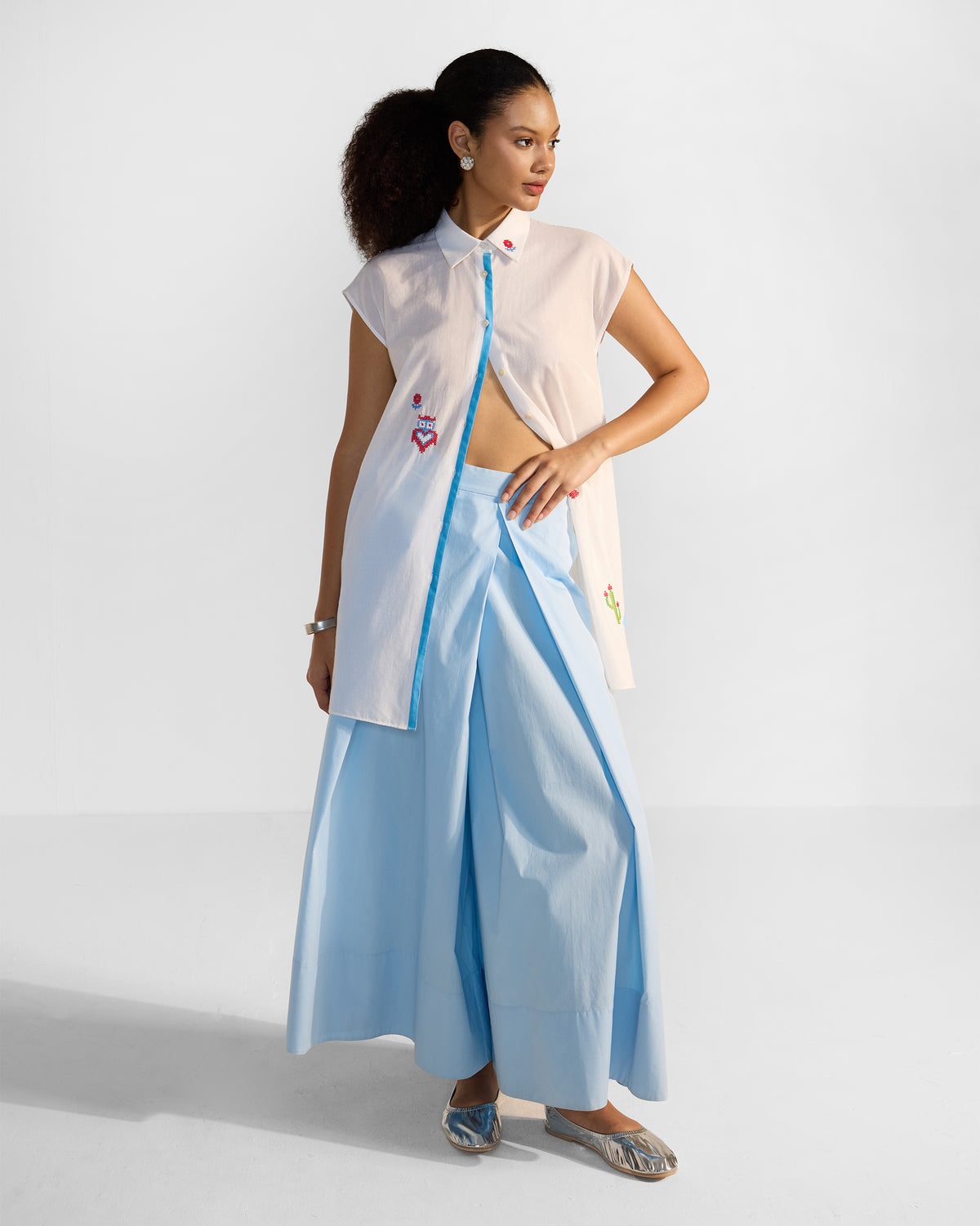 Person wearing a long white Eira top with blue trim and embroidery.