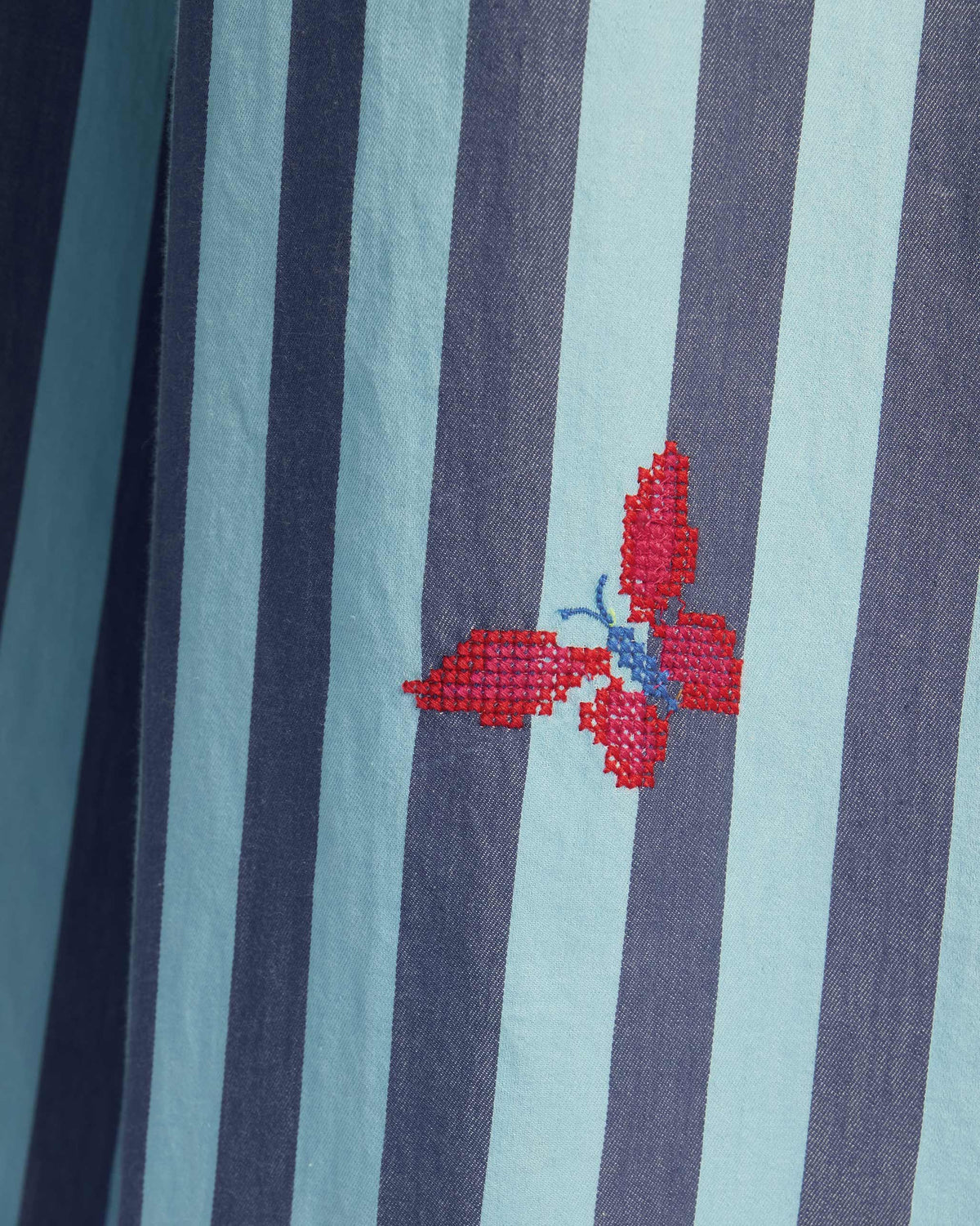 Close-up of a pink butterfly embroidery on a blue stripe Bargi jumpsuit.