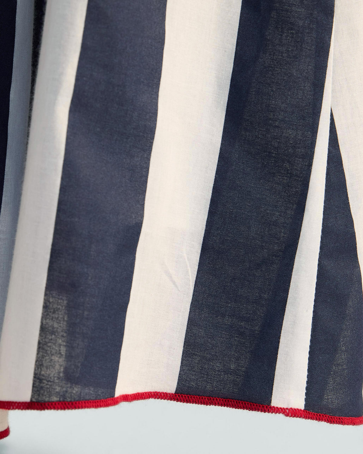 Close-up of navy and white stripe fabric with a red hem on a Reyat skirt.