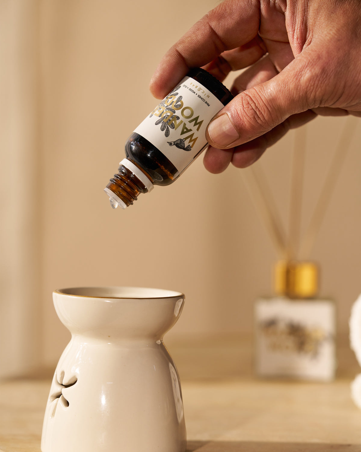 Hand tipping Wanderwood oil into a ceramic oil burner.