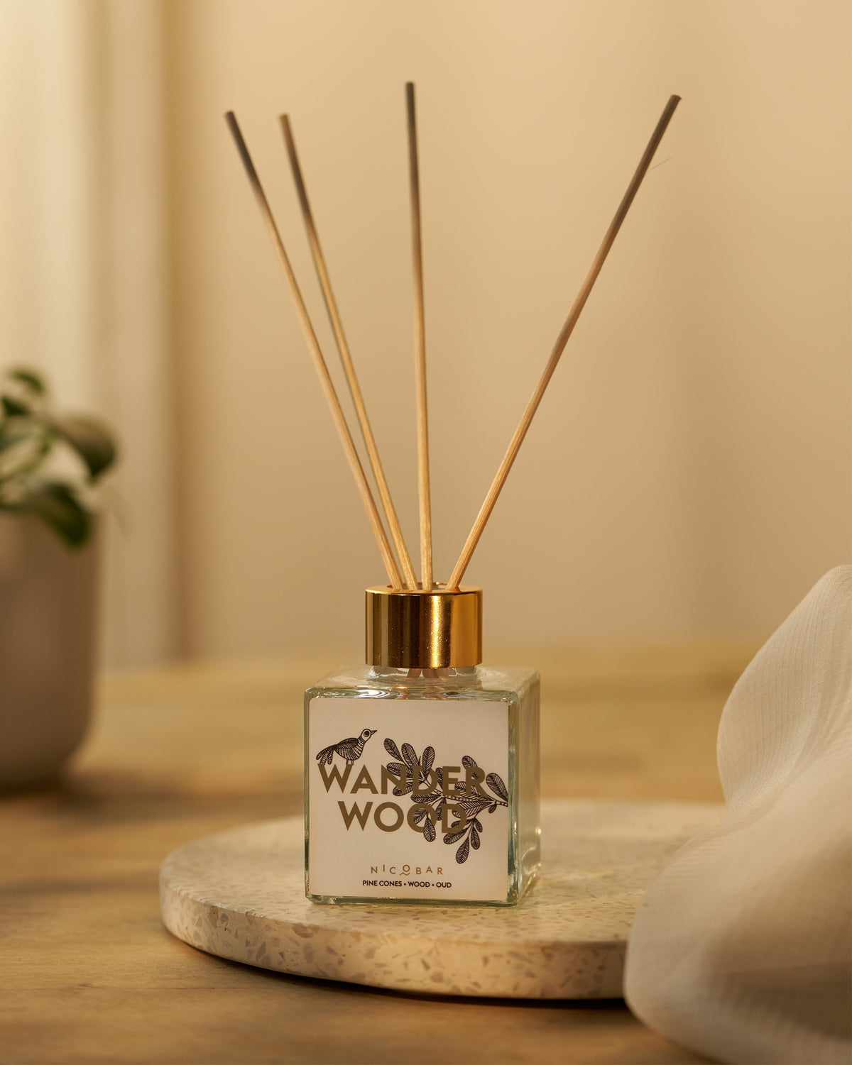 Wanderwood reed diffuser with gold collar and reeds on a stone tray.