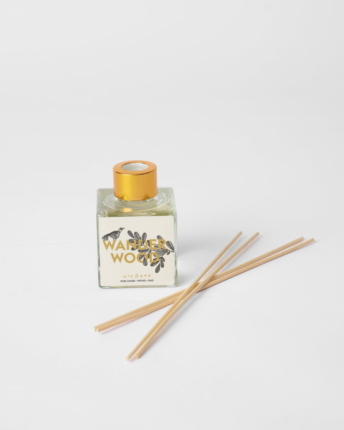 Wanderwood reed diffuser bottle with gold cap and reeds laid beside it.