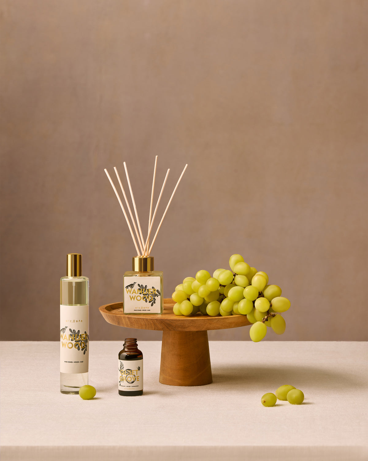 Wanderwood reed diffuser on a wooden stand beside other home fragrance bottles.