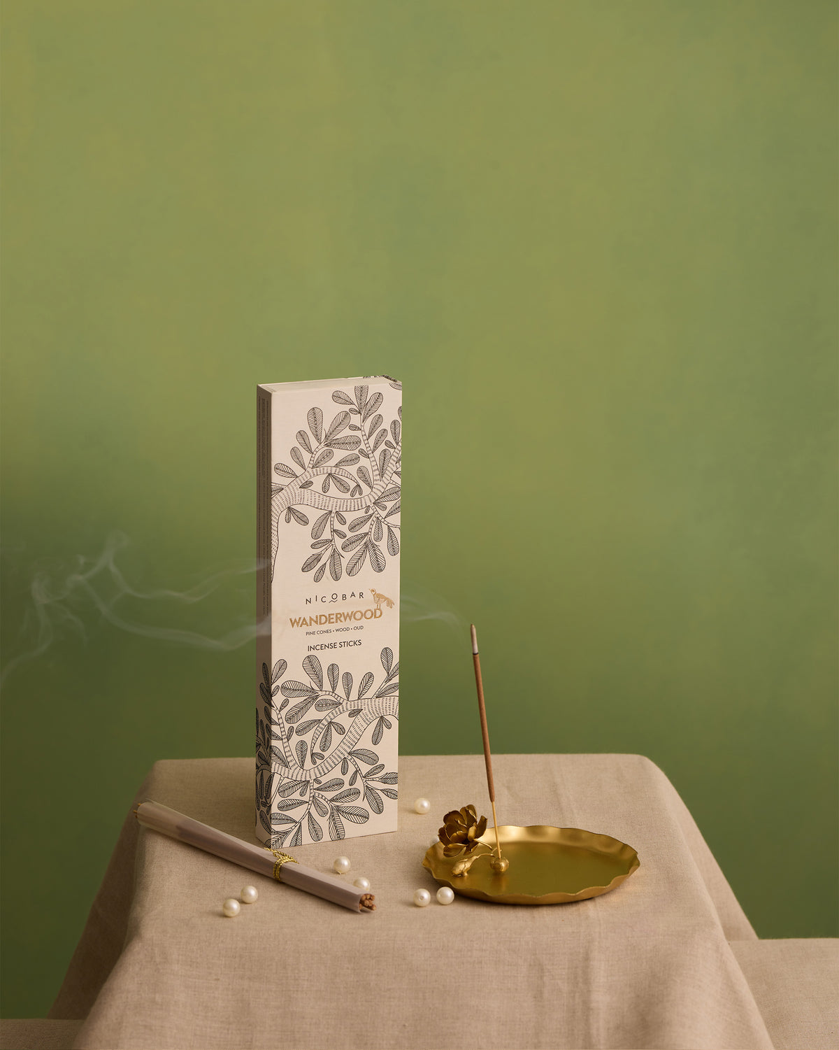 Wanderwood incense stick burning in a gold holder beside its box.