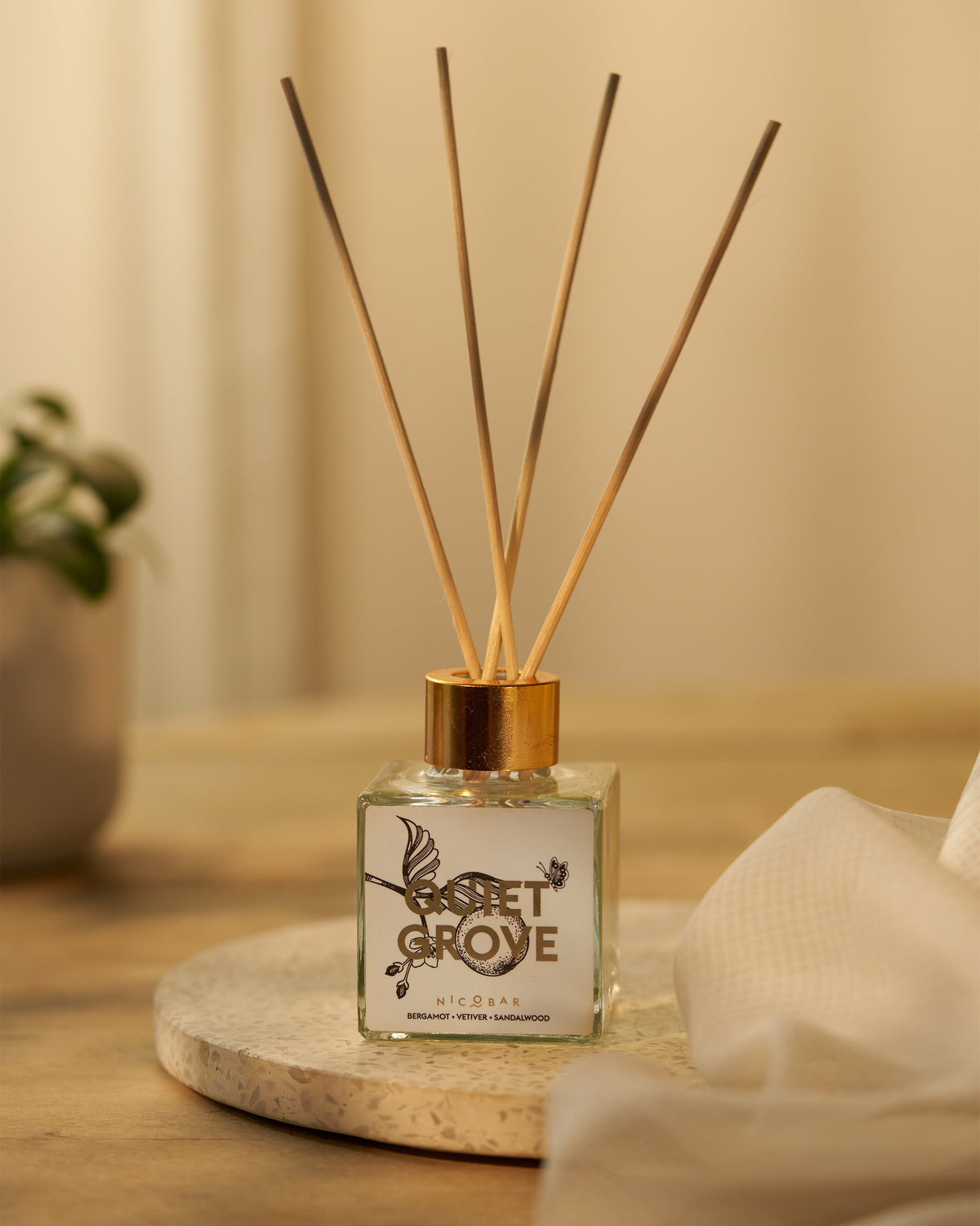 Quiet Grove reed diffuser with gold cap on a stone coaster.