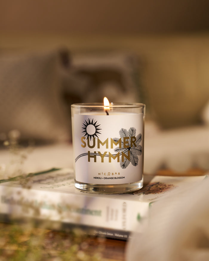 Lit Summerhymn candle in clear glass with a sun and leaf motif on the label.