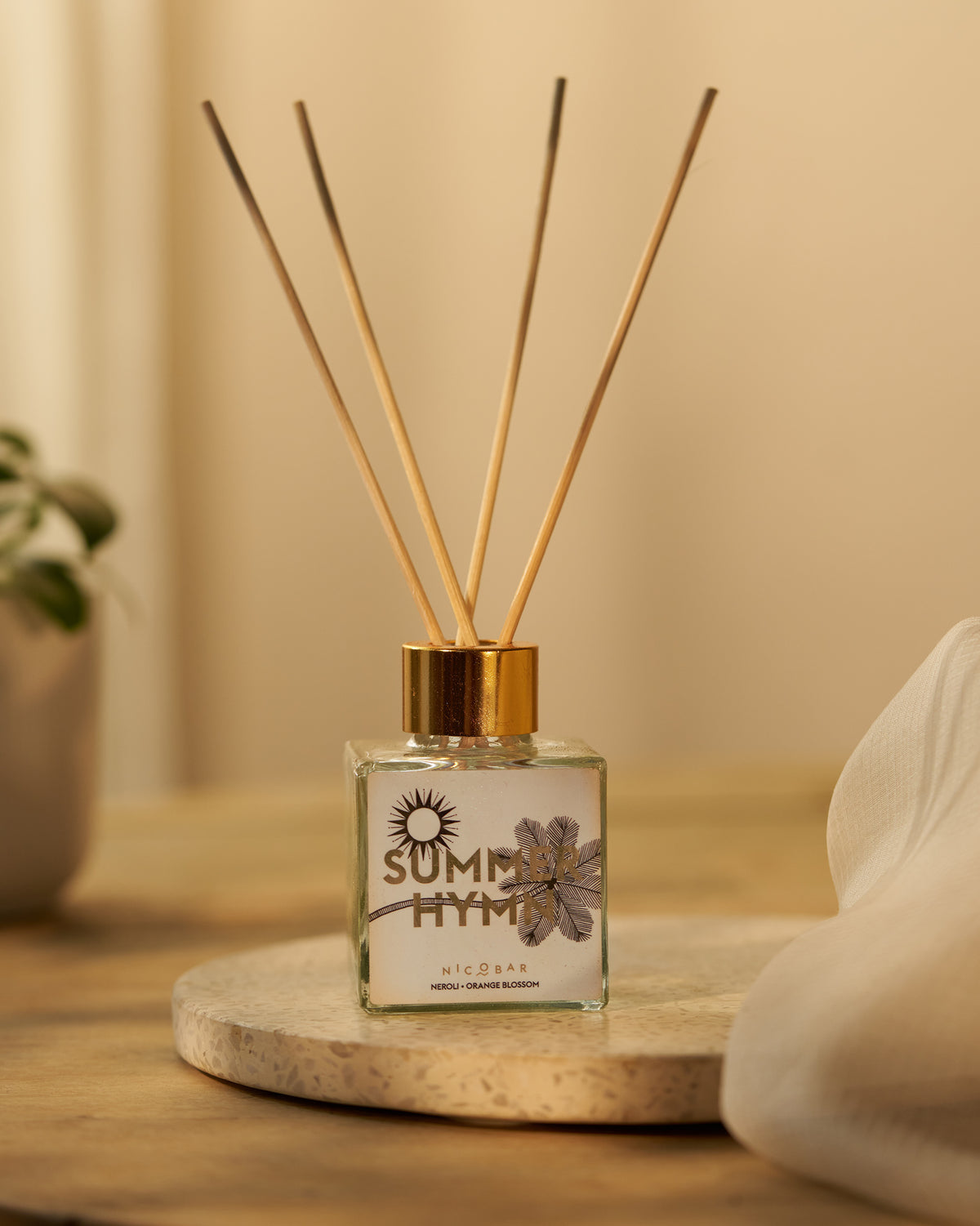 Summer Hymn reed diffuser with gold cap and wood reeds on a stone tray.