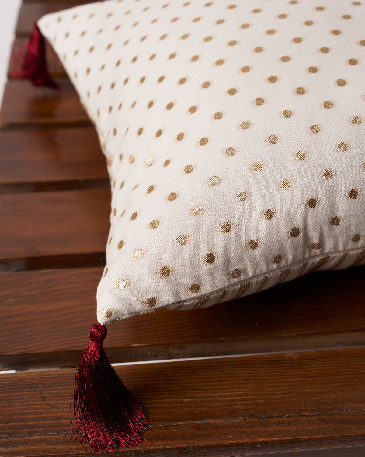 Close-up of Dottie Cushion Cover showing gold dots and a maroon tassel.