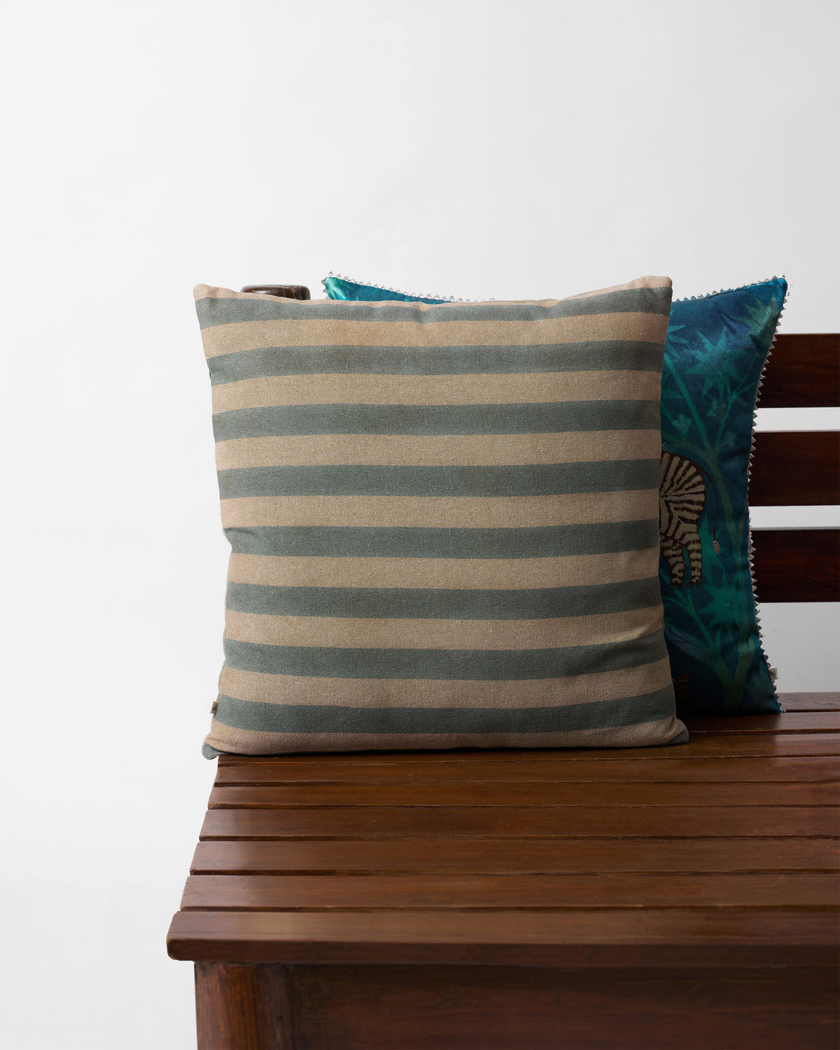 Pomme Cushion Cover in grey and cream stripes, shown on a bench.
