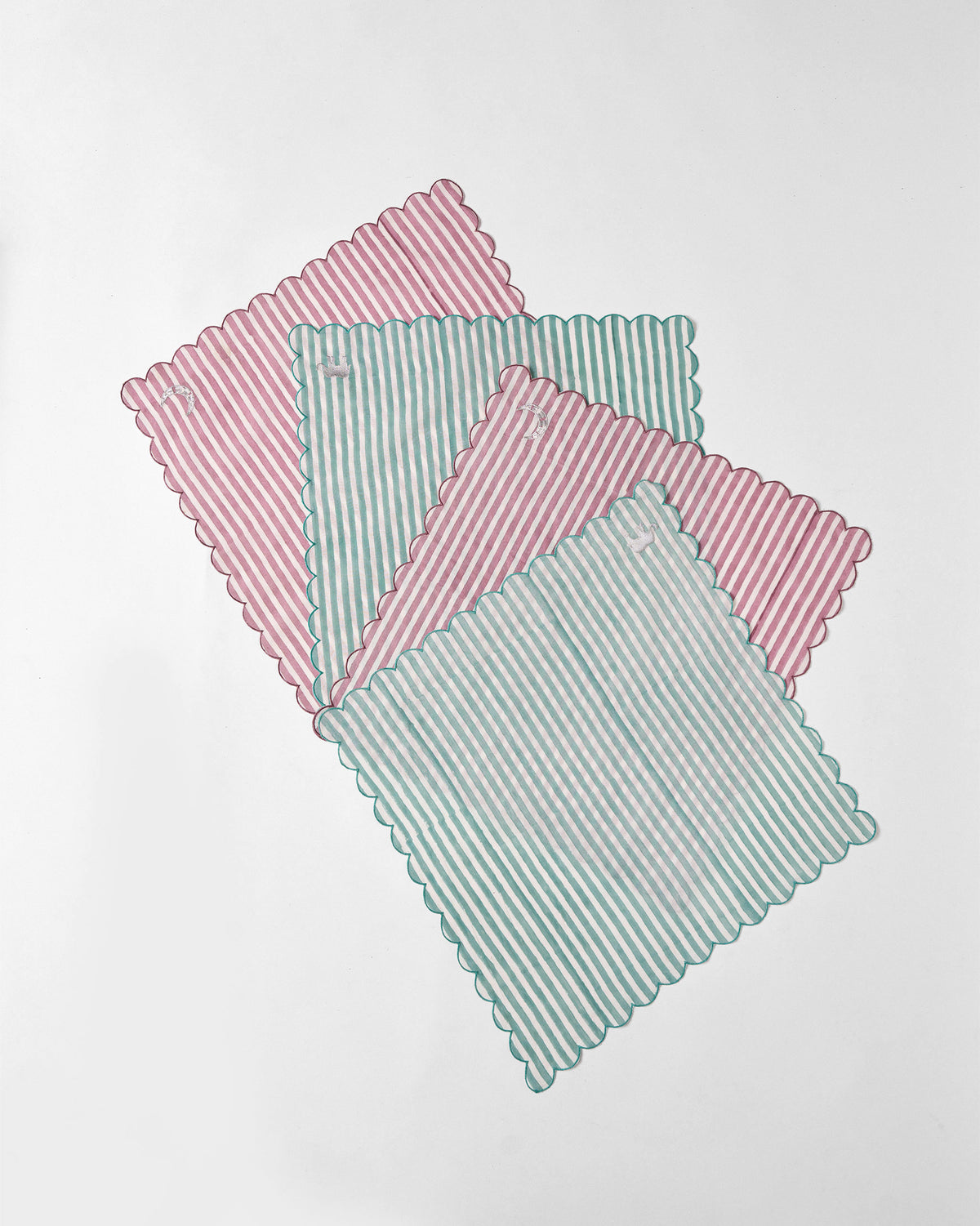 Set of four Yamuna napkins in pink and teal stripes with scalloped edges.