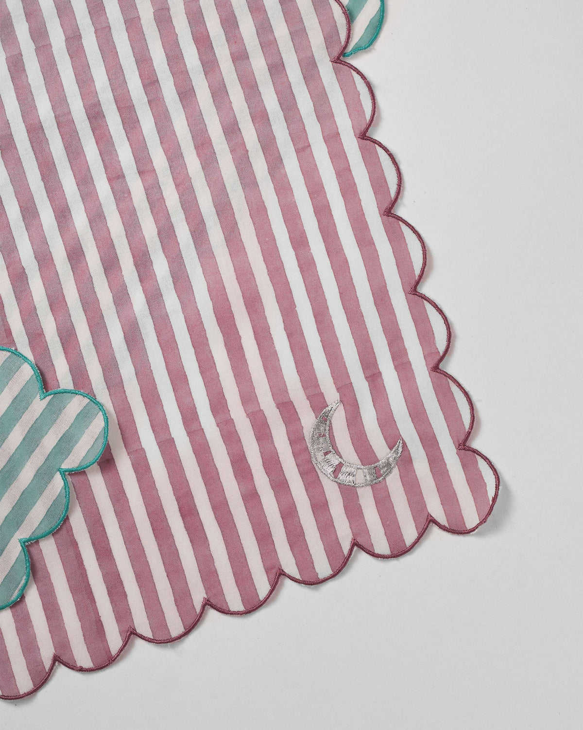 Close-up of a pink striped Yamuna napkin with a crescent moon embroidery.
