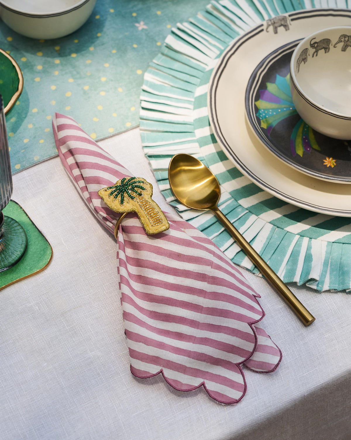 Pink striped Yamuna napkin folded through a gold palm napkin ring.