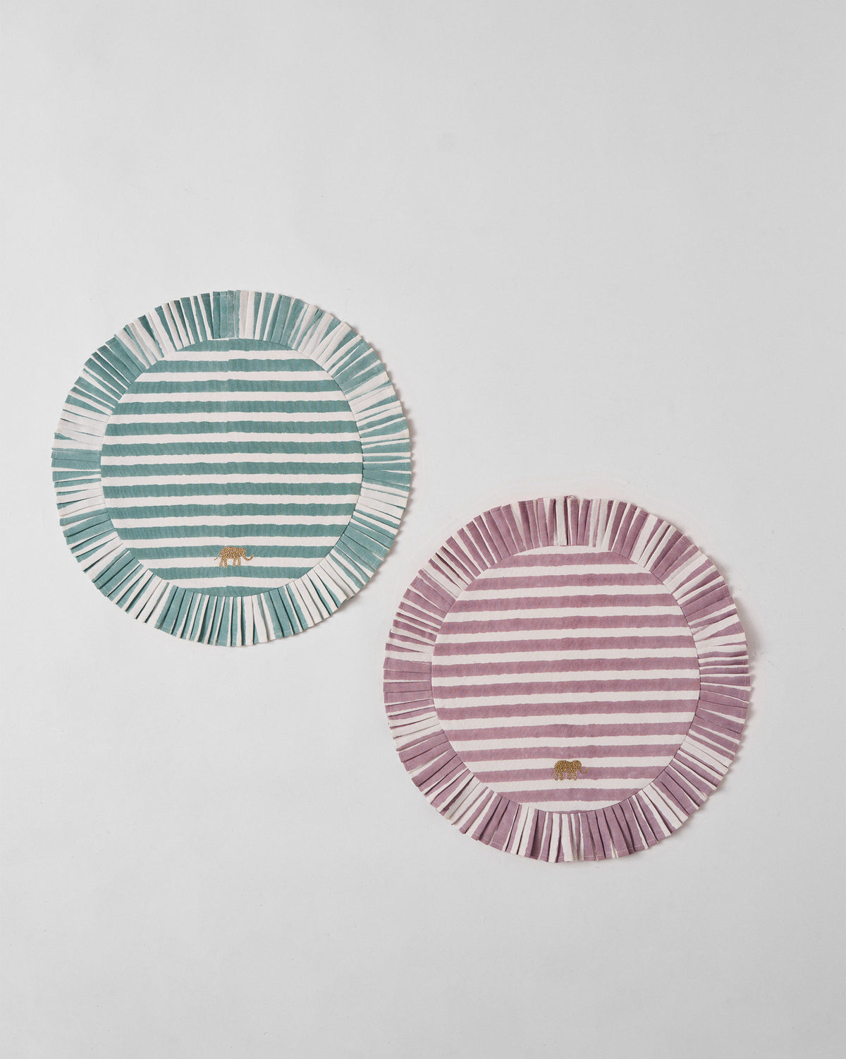 Pair of round Yamuna placemats in teal and mauve stripes with fringed edges.