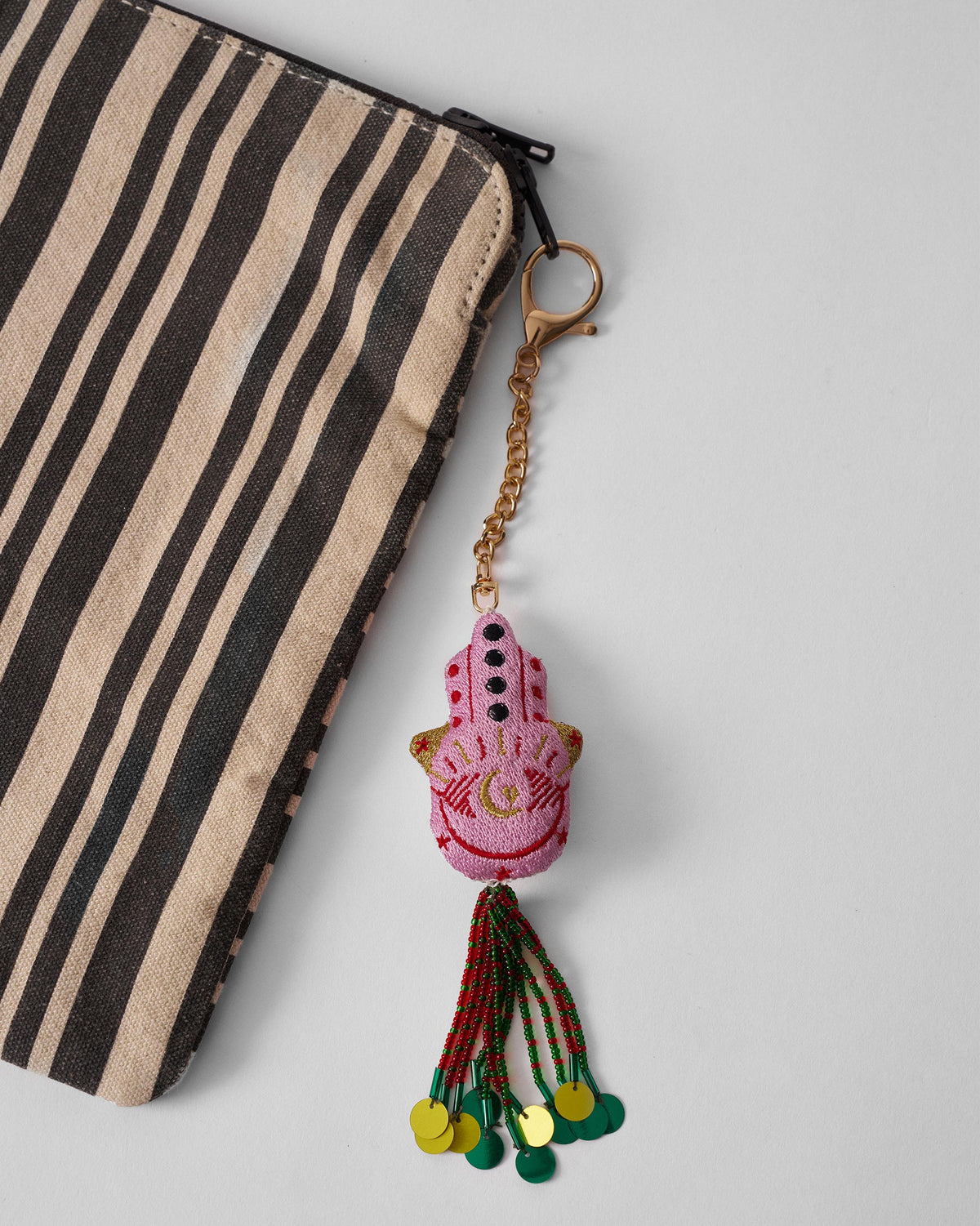 Hamsa Charm in pink hanging at an angle, with a beaded tassel.