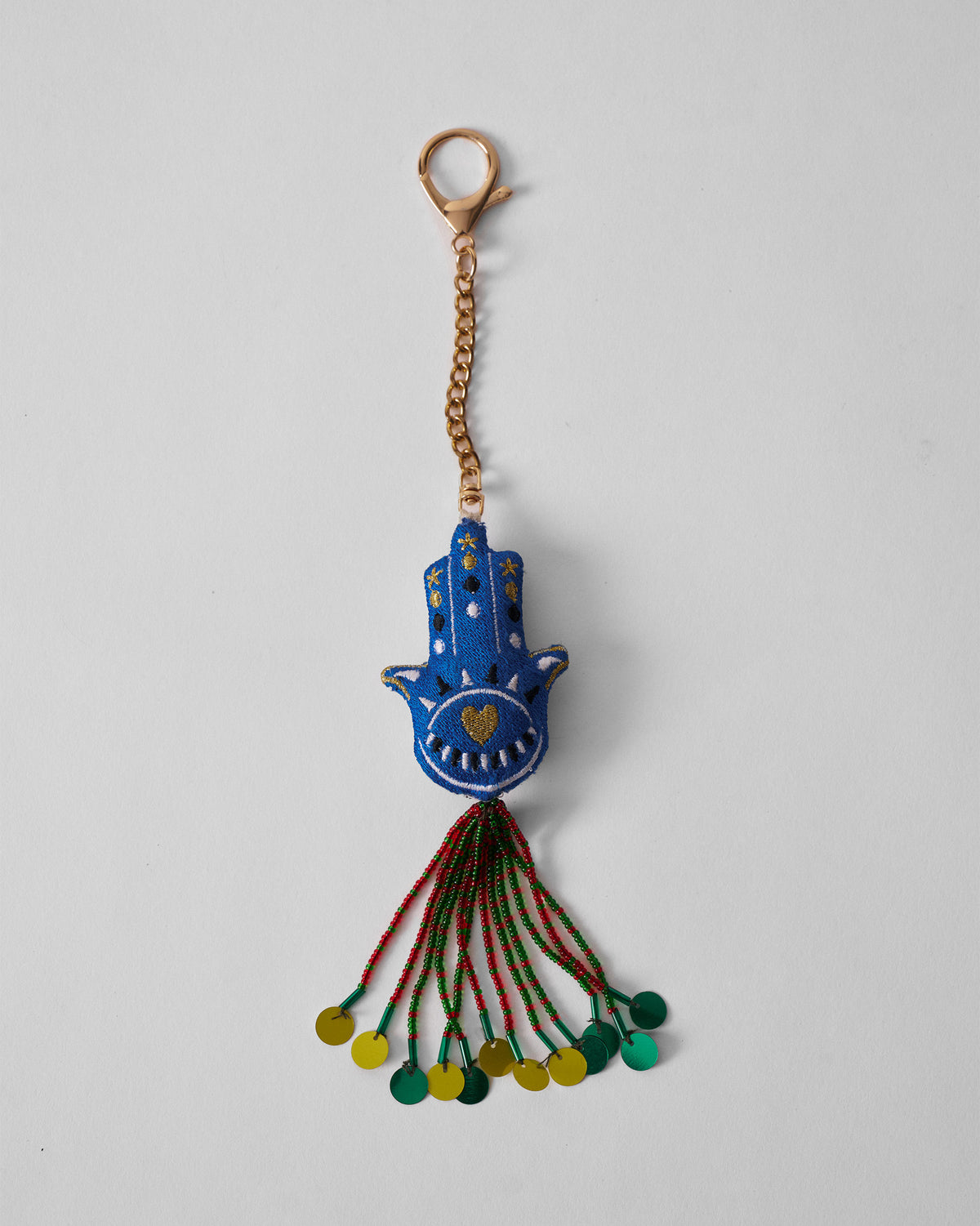 Hamsa Charm in blue hanging full length on a gold chain with beaded tassel.