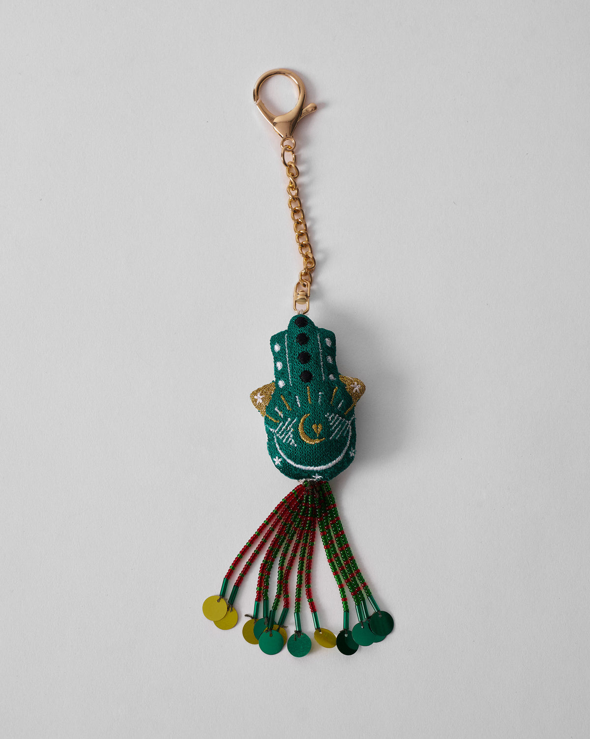 Hamsa Charm in green hanging full length on a gold chain with beaded tassel.