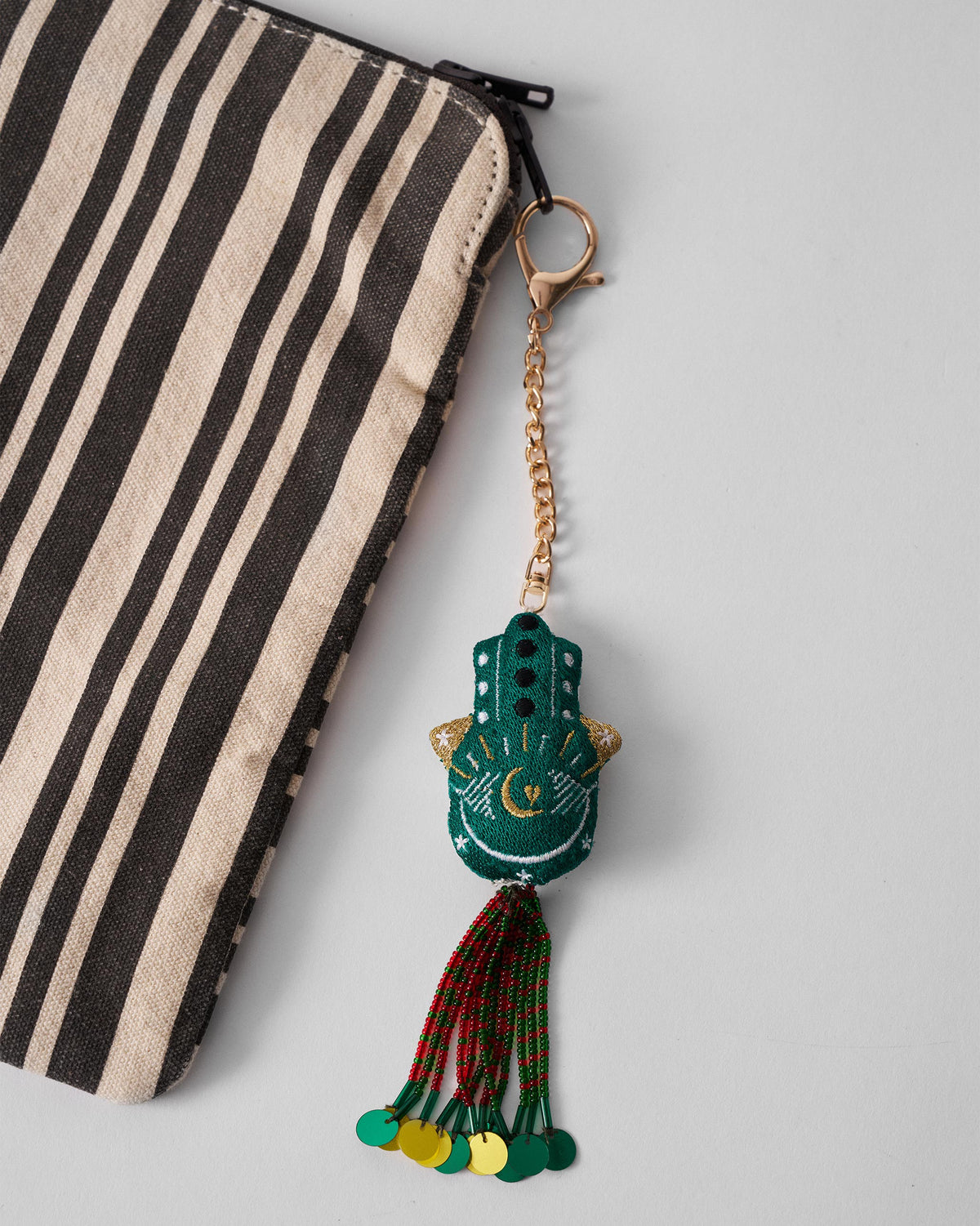 Hamsa Charm in green hanging at an angle, with gold accents and a beaded tassel.