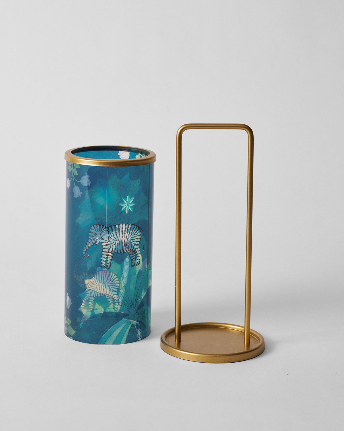 Palm Bloom lantern glass sleeve with jungle print beside its gold metal stand.