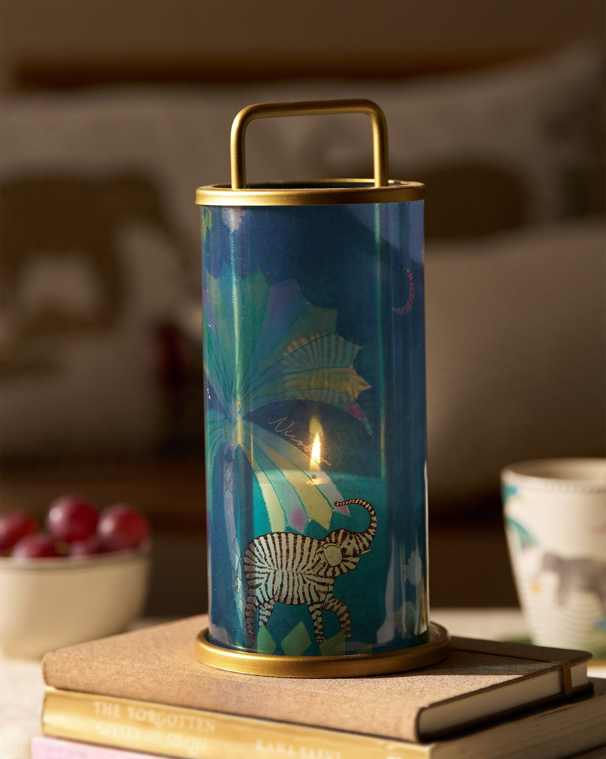 Lit Palm Bloom lantern with elephant motif glowing on a stack of books.