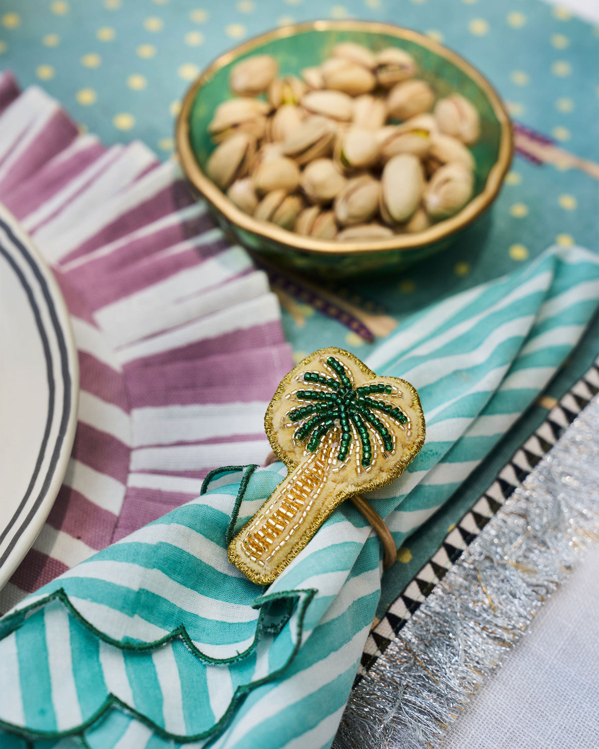 Palm napkin ring holding a teal striped napkin at a place setting.