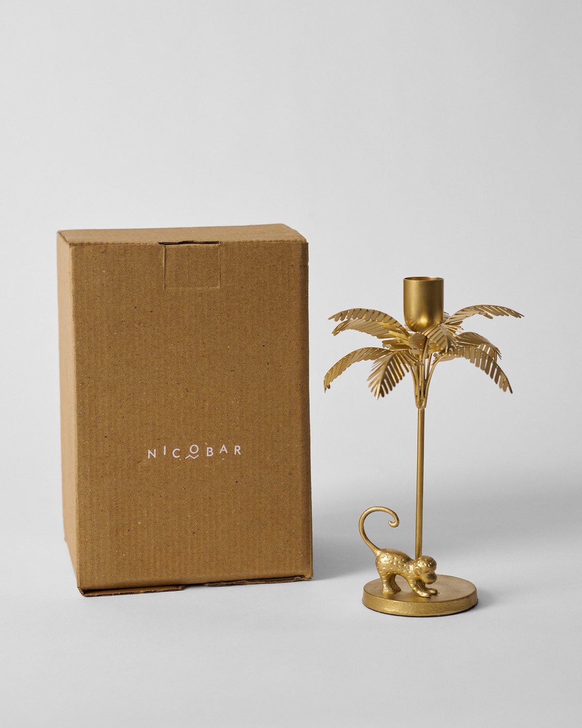 Gold Palm Bloom candle holder standing beside its brown Nicobar box.
