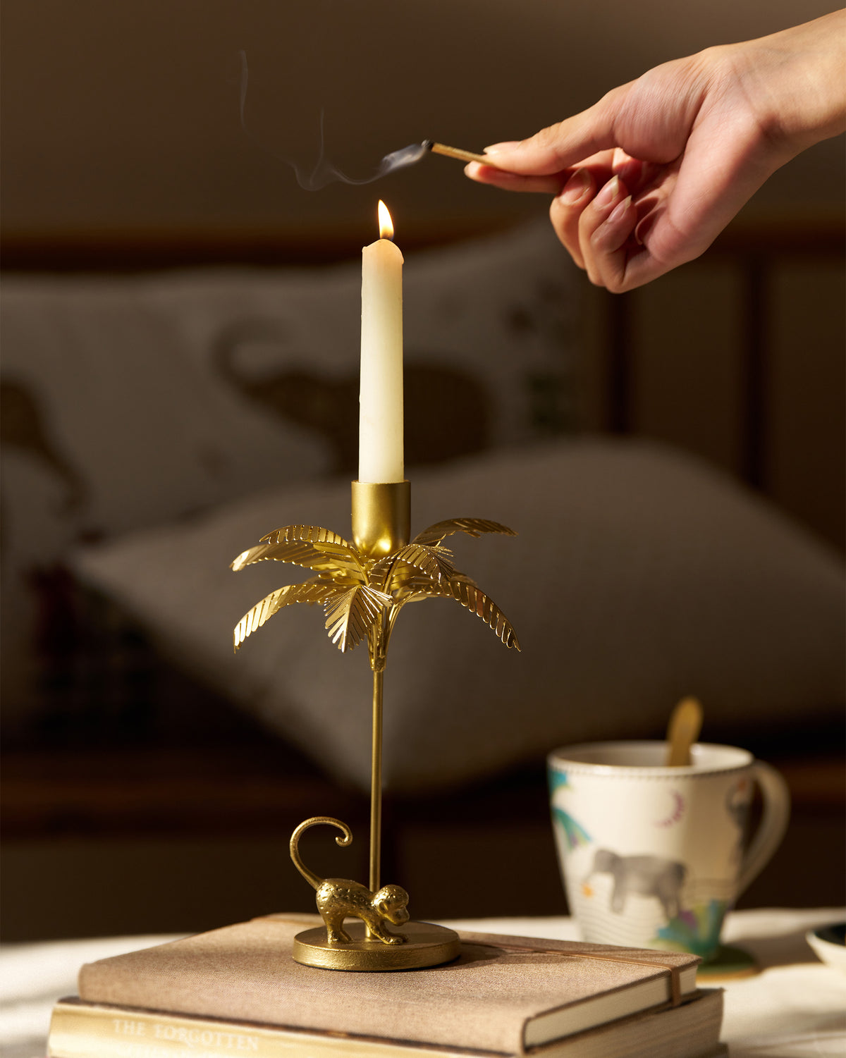 Gold Palm Bloom candle holder with a lit taper on a stack of books.