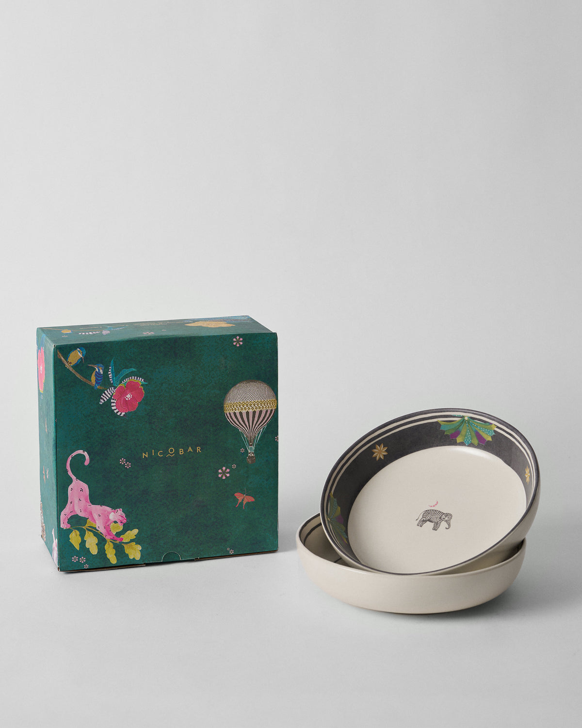 Palm Bloom shallow bowls stacked beside a teal Nicobar gift box.