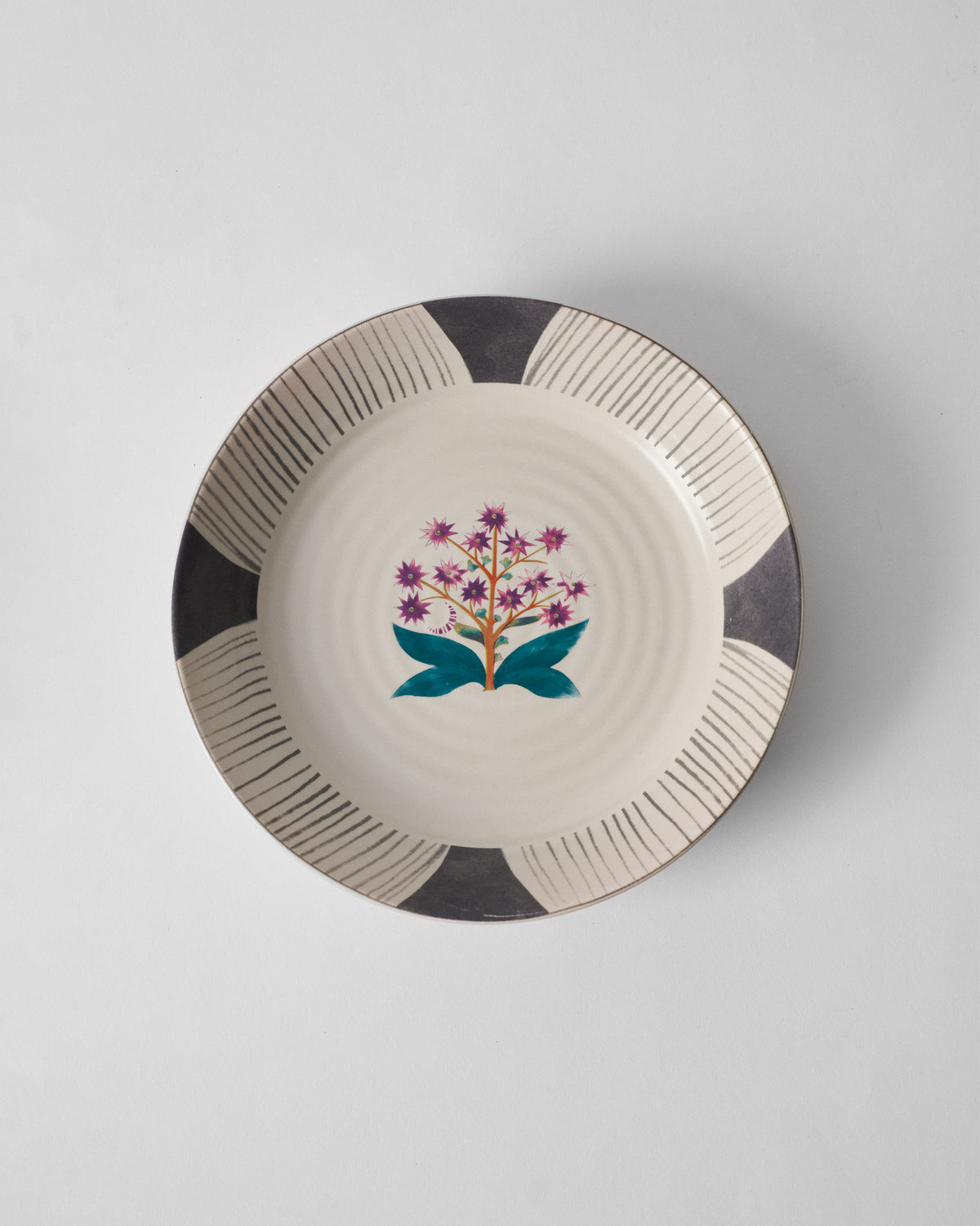 Overhead view of a Mogra pasta plate with a purple flower and teal leaves.