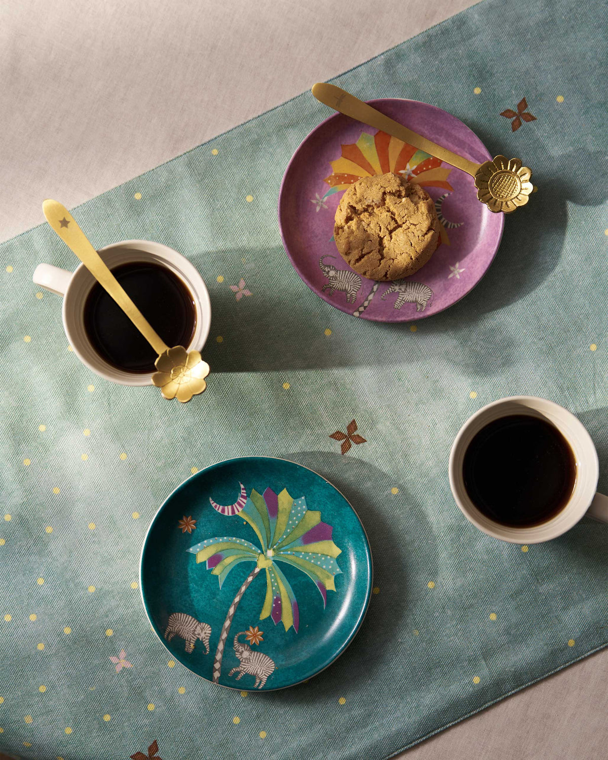 Palm Bloom tea plates with cookies beside cream coffee mugs.