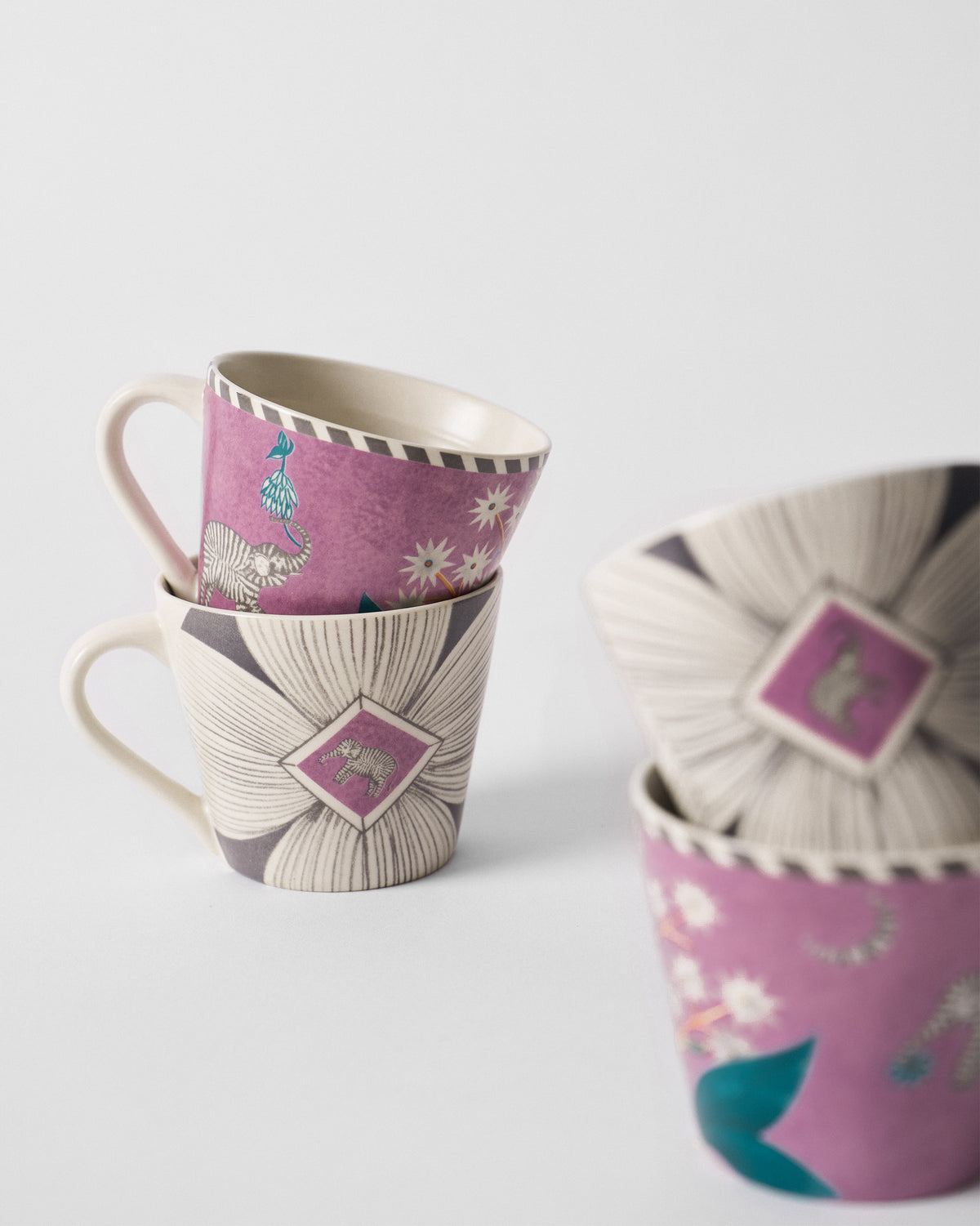 Stacked Mogra Bloom espresso mugs showing a magenta elephant motif over a cream floral print.