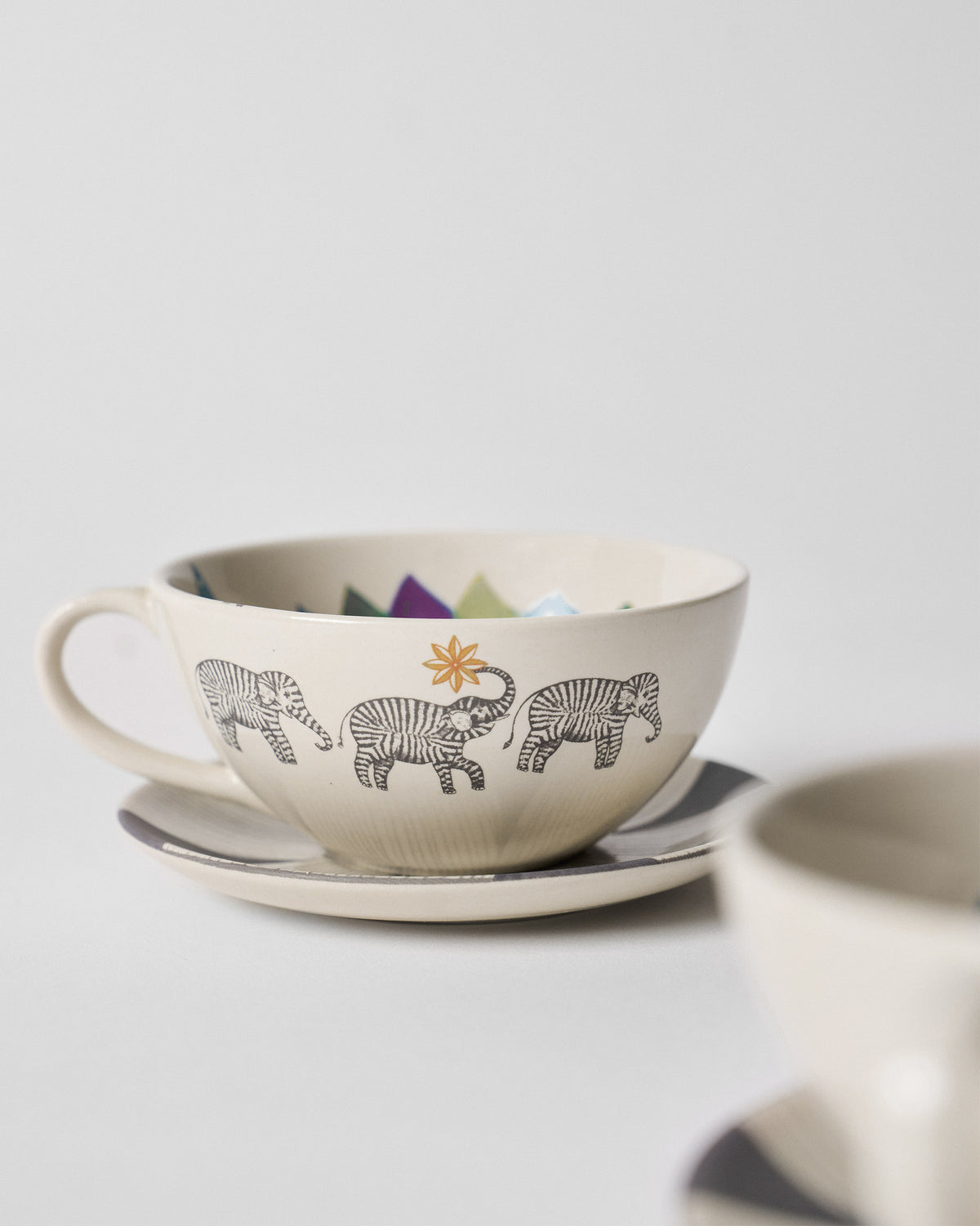 Close-up of a Palm Bloom coffee cup with three striped elephants and an orange sun.