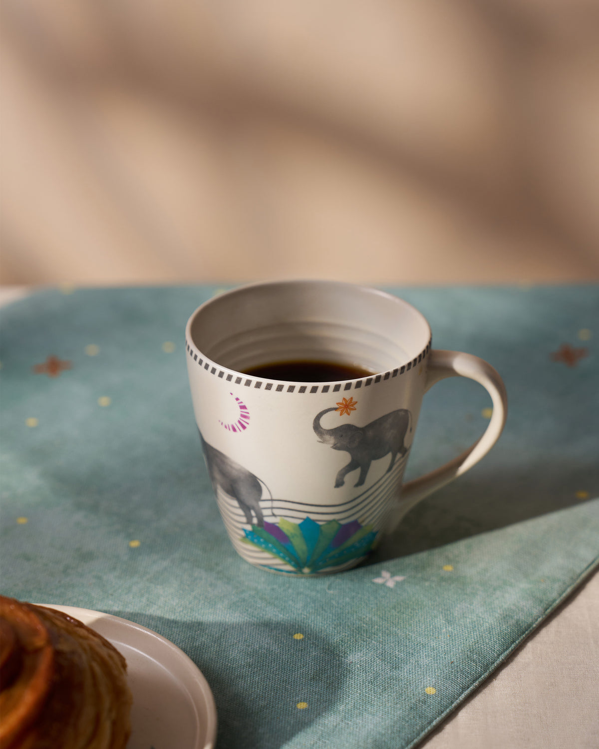 Tusk Conical Mug filled with coffee, with elephant motifs and a dotted rim band.