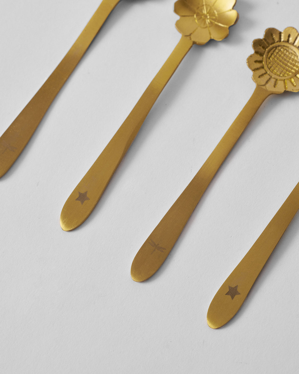 Close-up of gold Phool coffee spoon handles with star and dragonfly stamps.