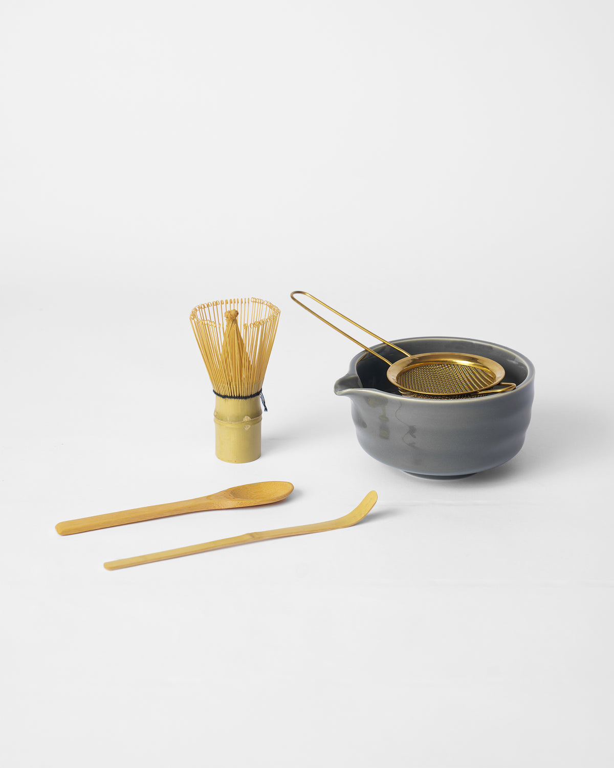 Grey spouted matcha bowl with a gold strainer, bamboo whisk, and scoops.